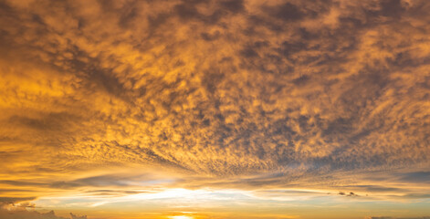 Colorful sunset sky with setting sun behind vivid orange and yellow clouds
