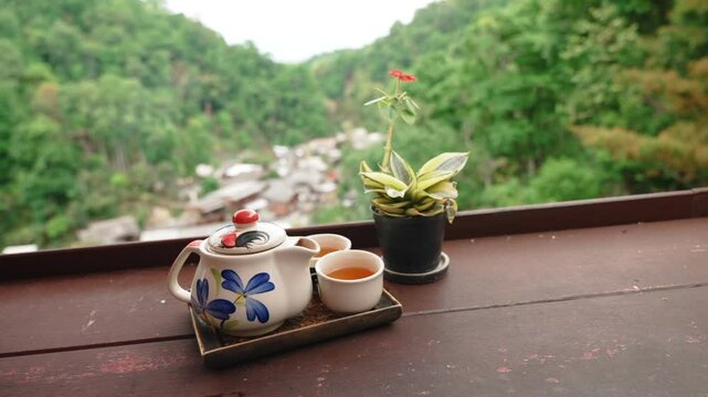 Close up of traditional tea set and potted plant on wooden table on outdoor cafe terrace in Mae Kampong hillside village with mountain view