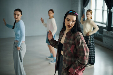 Young women rehearsing dance routine in spacious room with large windows, each performing...
