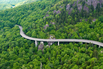Road trip driving on Linn Cove Viaduct in Appalachian mountains. Winding parkway in mountain forest with green canopies in summer rain season