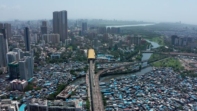 Stunning Aerial view of Mumbai showing a stark contrast between high-rise buildings and the dense slums of Dharavi, with a metro line, river, and city infrastructure in view.