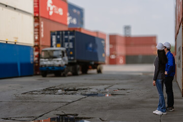 Fototapeta premium Industrial engineer standing at shipping container yard inspecting cargo delivering loading as plan. Woman manager and diverse ethnic worker checking import export container at logistic terminal dock.