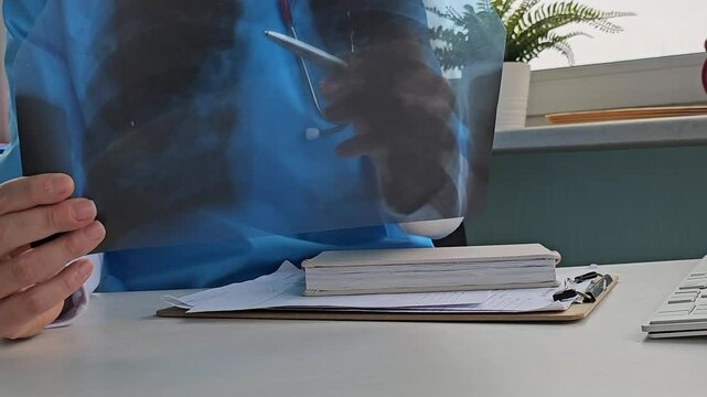 Doctor examines X-ray lung,   results in clinic while taking notes during consultation