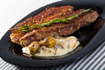 Roasted veal steak with delicious creamy mushroom sauce and rosemary on striped textile surface
