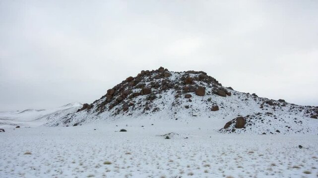 Snow covered rocky hill in middle of desert on cloudy day