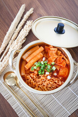 Close-up of homemade Korean tteokbokki, spicy ramyeon noodles, and odeng fish cakes served in a golden pot, with golden chopsticks and spoon placed beside it. Captured with natural window light.
