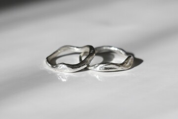 Two unique handmade silver rings free form elegantly displayed on smooth white surface. 