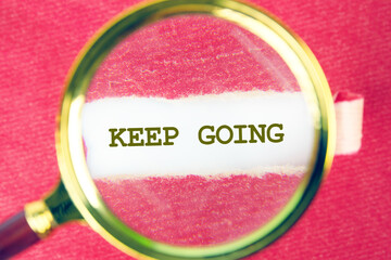A magnifying glass magnifies the phrase keep going printed on a piece of paper, set against a...