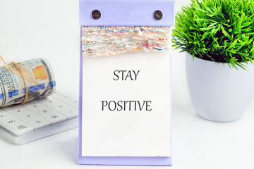 A motivational note displaying stay positive sits on a desk next to a calculator and a potted...
