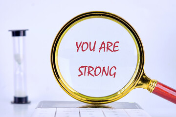 A magnifying glass focuses on the words you are strong, highlighting a positive affirmation. An...