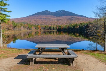 Obraz premium Autumnal lake scene with mountain reflection and picnic table