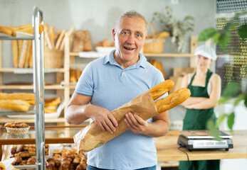 Portrait of male customer holding paper bag of fresh baguettes in bakery interior