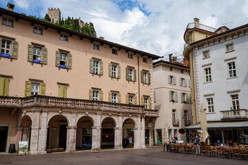 Naklejka premium Piazza 3 Novembre in the historic center of Arco, Trentino-Alto Adige, South Tyrol, Italy. A lively square with historic buildings and cafés. Above it towers the castle ruins, the town's landmark.