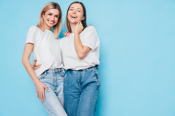 Naklejka premium Two young beautiful smiling brunette hipster female in trendy summer clothes. Lovely women posing on blue background in studio. Positive models having fun. Cheerful and happy. isolated