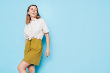 Young beautiful smiling blond female in trendy summer yellow dress clothes. Carefree woman posing near blue wall in studio. Positive model. Cheerful and happy, isolated