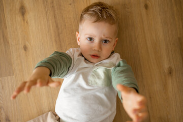 Young child lying on wooden floor reaching towards the camera with an innocent gaze