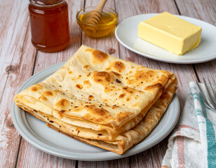Moroccan msemen bread layered and folded on a plate served with honey and butter