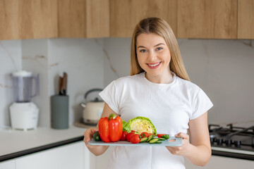 Smiling woman holds fresh vegetables in home kitchen for healthy eating