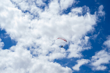 Paraglider Flying High Among White Clouds in a Bright Blue Sky