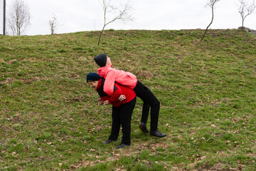 Two friends playfully enjoying a piggyback ride on a grassy hill during a cloudy day in a serene...
