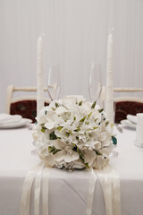 a banquet table at a wedding celebration served with dishes and decorated with two tall candles and a bouquet of white roses for the bride between them