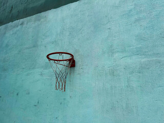 A weathered basketball hoop stands out against a textured blue wall, capturing the essence of urban courts and still moments in sports culture.