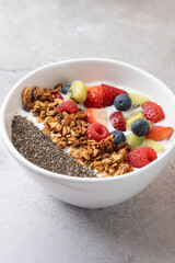 White bowl with healthy breakfast: kefir, assorted fruits, homemade granola and chia seeds. Light stone background. Concept of clean eating and daily wellness