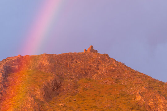 View of a mountain at sunset with the ruins of a medieval castle crossed by a rainbow