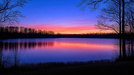 Serene lake sunset with vibrant colors reflected on the water.  Silhouette trees frame the tranquil scene