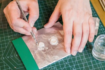 Close-up of hands working with silver clay with a fine brush, showcasing precision and detail.