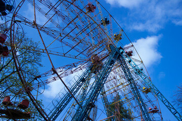 Abandoned Old Ferris Wheel Against a Bright Blue Sky with White Clouds