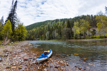 Experience the serene beauty of a river landscape featuring a kayak resting on a rocky shoreline,...