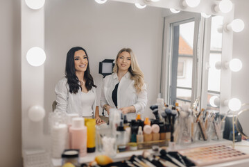 Two smiling make-up artists posing at their workstation with cosmetics and tools