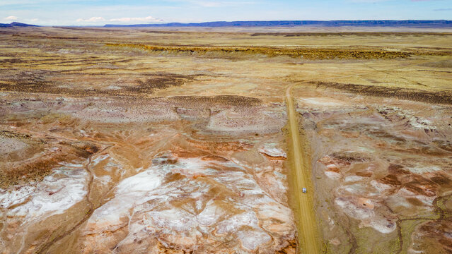 Aerial view of a van on a dirt road crossing colorful desert terrain
