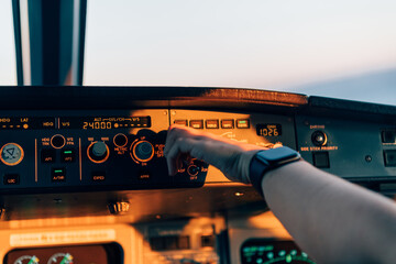 Pilot adjusting autopilot controls in aircraft cockpit during sunset
