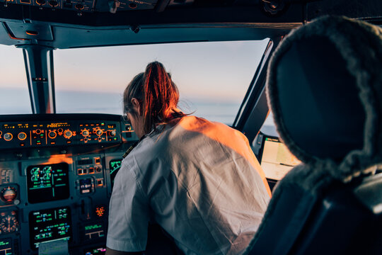 Female pilot operating aircraft cockpit during sunset flight