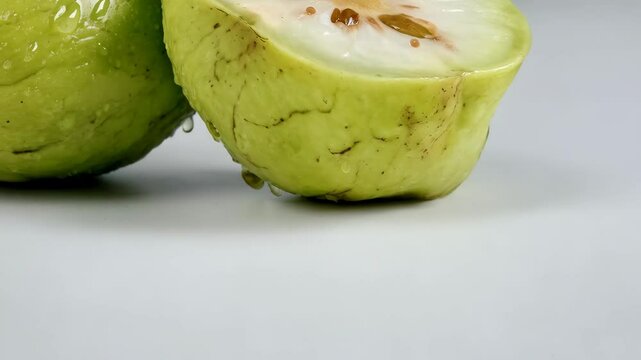 Closeup of fresh green bael fruit cut in half, seeds visible and droplets on smooth rind, isolated on plain white background
