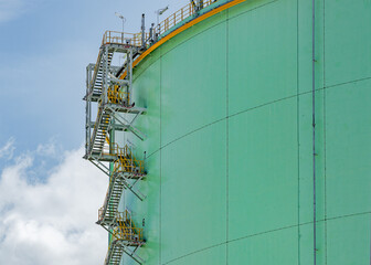An image of a tall, cylindrical, green industrial storage tank with a metal staircase equipped with...
