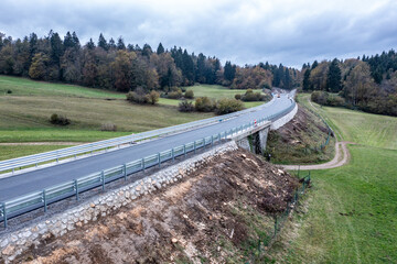 Newly Constructed Highway Crossing Fields with Underpass Beneath, Featuring Fresh Asphalt and Aluminum Road Barriers Under Cloudy Sky

