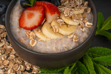 Cooked spelt in bowl. Oatmeal milk porridge with fruits and berries on dark background