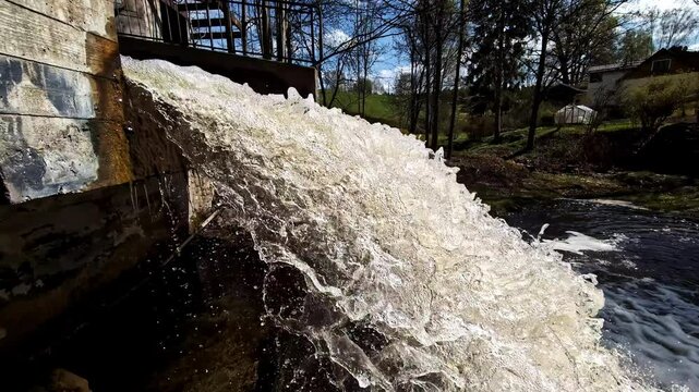 Waterfall water rushes from dam structure in creating foamy cascade