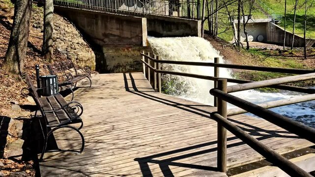 Wooden terrace with benches overlooking dam waterfall in Smiltene on Abuls river
