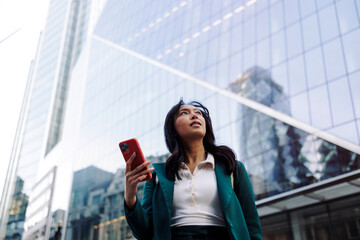 Businesswoman with smartphone looking up in urban cityscape