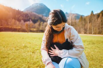 Girl holding black cat in sunny mountain field