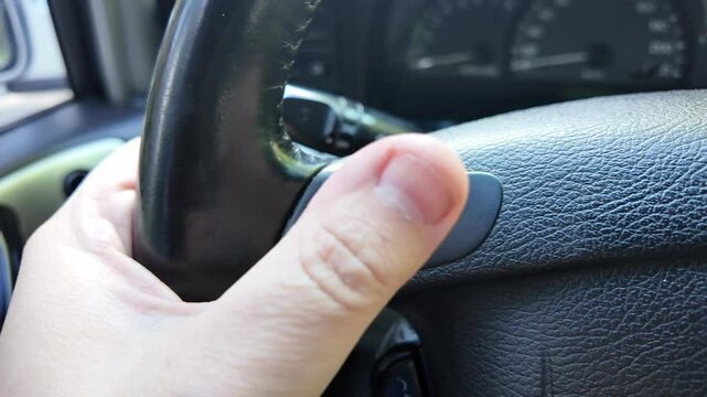 The driver presses the horn. The driver honks while driving. The driver holds the steering wheel.