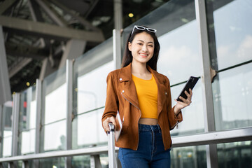 Happy young asian woman traveler using smartphone and holding boarding pass while standing at the airport terminal ready for vacation trip, smiling female tourist with confidently travel insurance