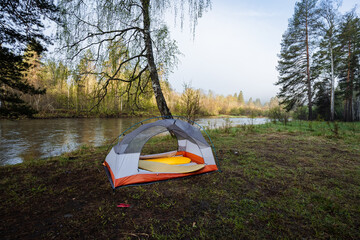 A tranquil and serene riverside camping scene featuring a cozy tent nestled under expansive, clear...