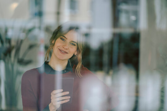 Smiling woman using smartphone in a caf� reflecting on window