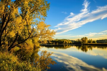 Obraz premium Serene autumn landscape. Golden trees reflected in calm lake water under a blue sky with clouds. Ideal for calendars, websites, travel brochures.