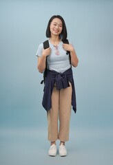 Young woman with a backpack poses confidently against a light blue background in a casual outfit...